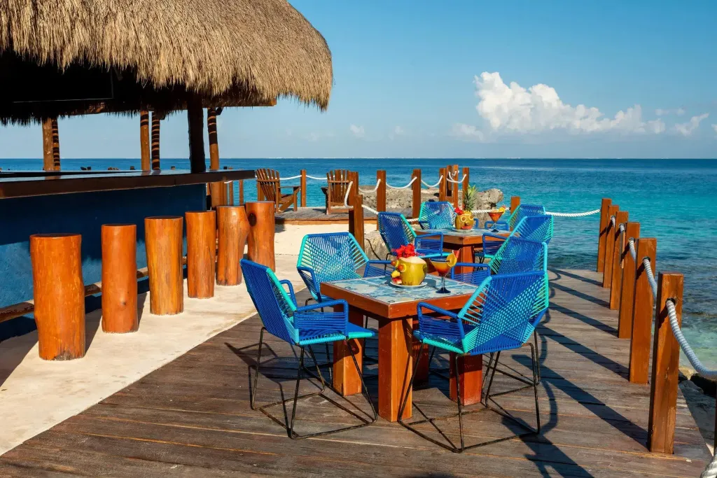 Terrasse en bois avec tables et chaises bleues donnant sur la mer turquoise.