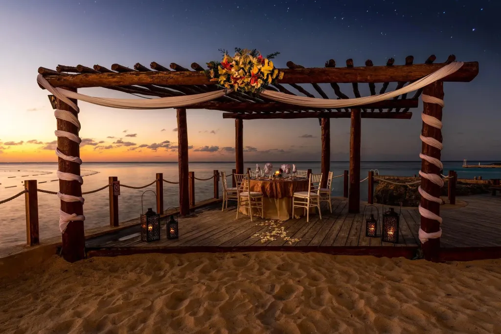 Une table dressée pour un dîner romantique sur une plage au coucher du soleil.