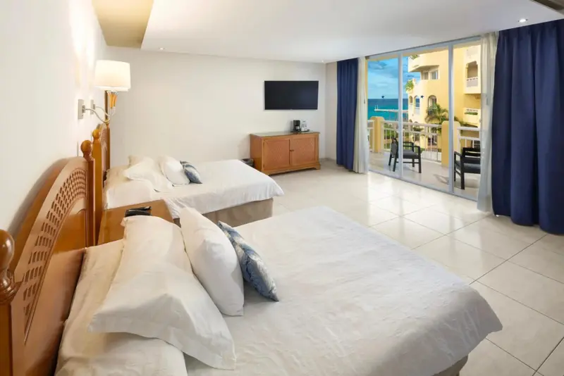 Une chambre lumineuse avec deux lits et une vue sur la mer par de grandes baies vitrées.