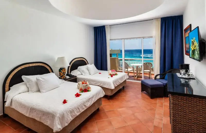 Chambre lumineuse avec deux lits et vue sur la mer depuis un balcon.