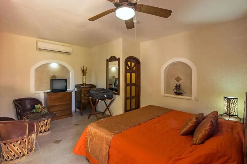 Une chambre lumineuse avec un lit recouvert d'une courtepointe orange et des meubles en bois.