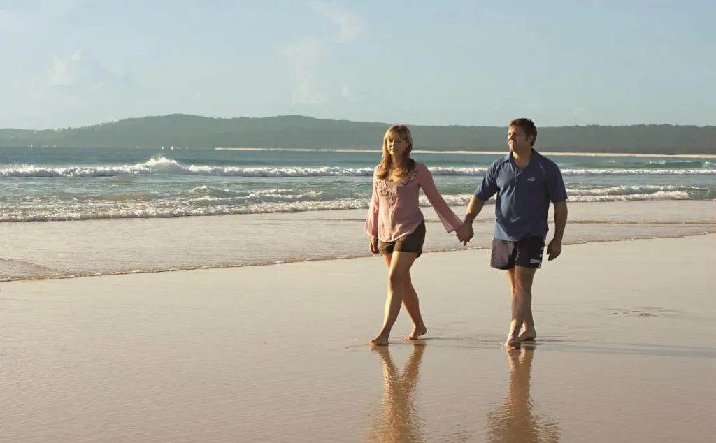 Un couple se promène main dans la main sur une plage de sable.