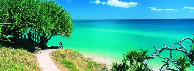 Vue panoramique sur une plage de sable fin et une mer turquoise sous un ciel bleu nuageux.