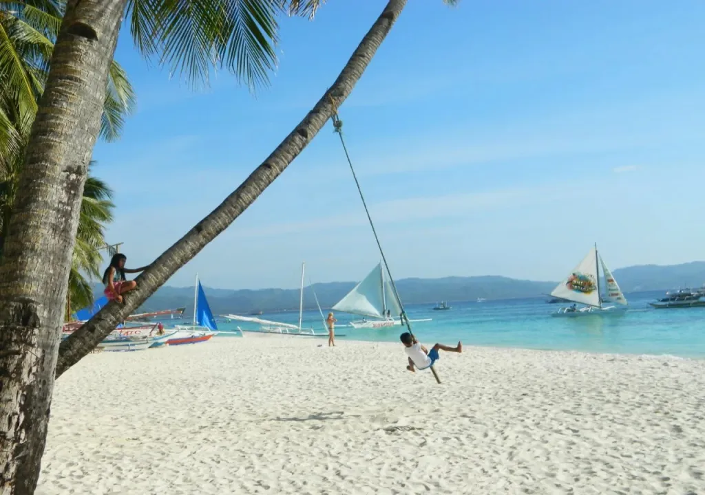 Une plage de sable blanc bordée de palmiers et de bateaux à voile.
