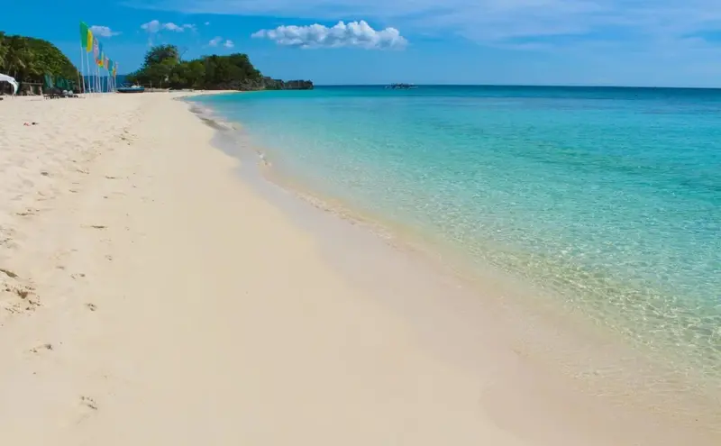 Plage de sable fin bordée d'une mer turquoise sous un ciel bleu.