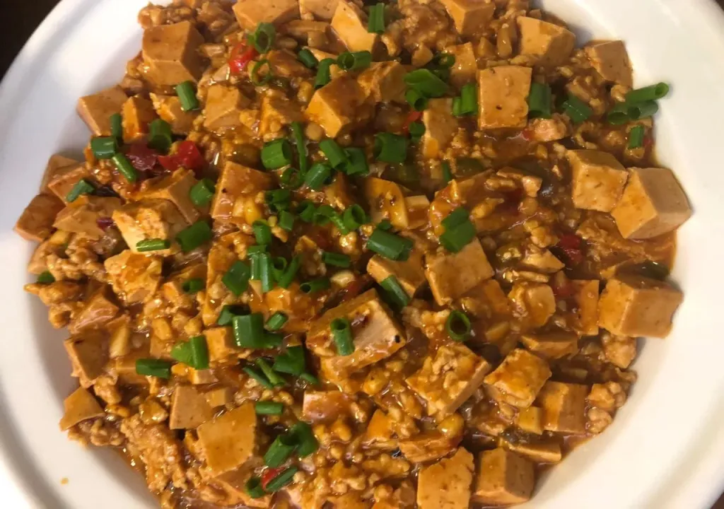 Plat de tofu épicé garni de ciboulette fraîche, servi dans une assiette blanche.