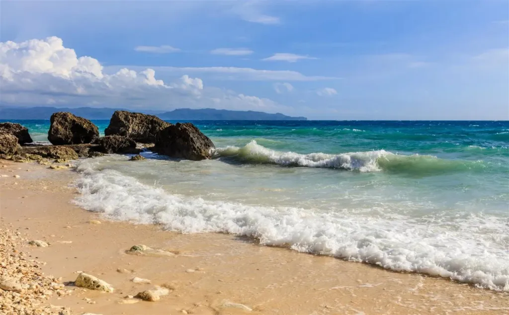 Une plage de sable fin bordée par une mer turquoise et des rochers.