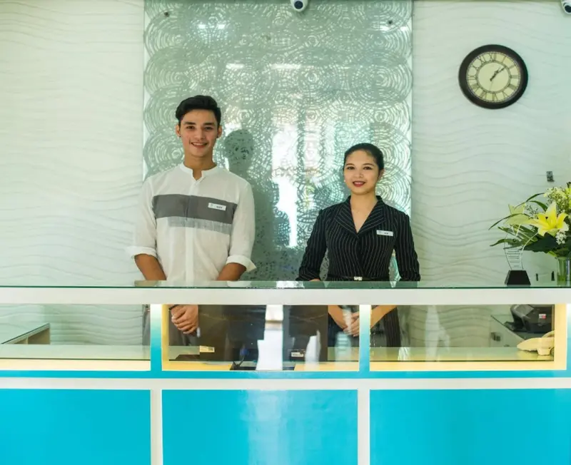 Deux employés souriants se tiennent derrière un comptoir d'accueil.