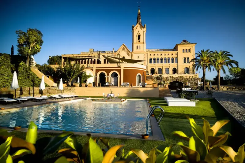 Une piscine rectangulaire au premier plan, avec un bâtiment historique en arrière-plan.