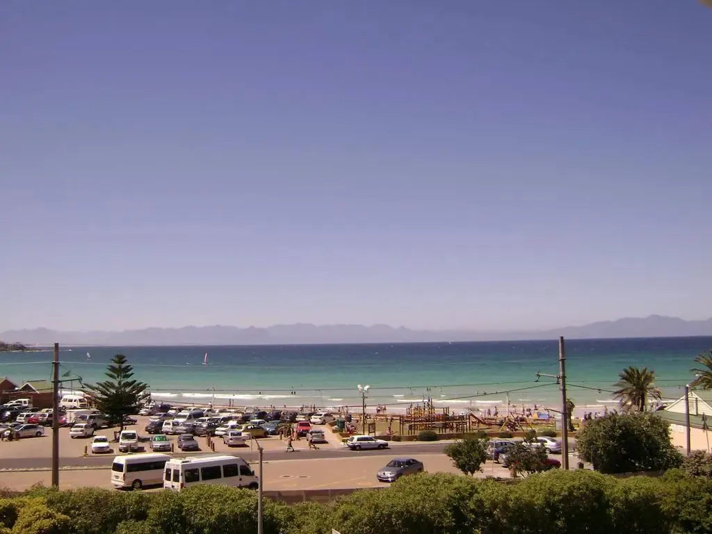 Vue d'une plage ensoleillée avec des voitures garées et des personnes se promenant.
