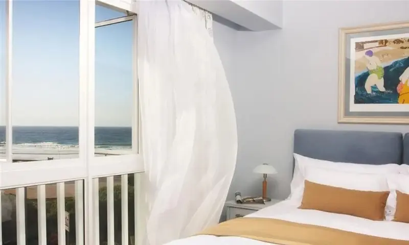 Une chambre lumineuse avec un lit et une vue sur la mer par une fenêtre ouverte.