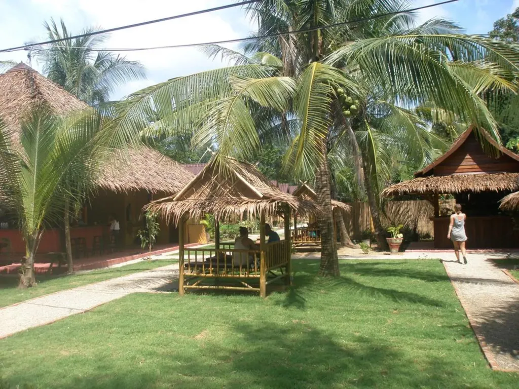 Deux personnes sont assises à une table en bois sous un abri de chaume dans un jardin tropical.
