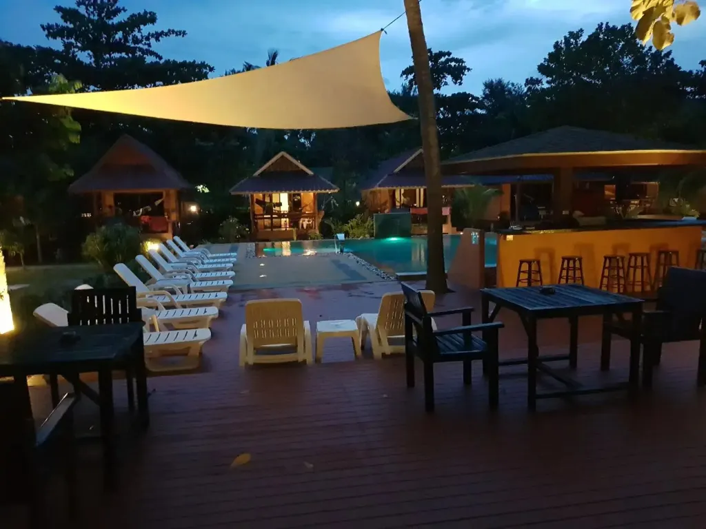 Terrasse en bois avec transats et tables près d'une piscine éclairée.