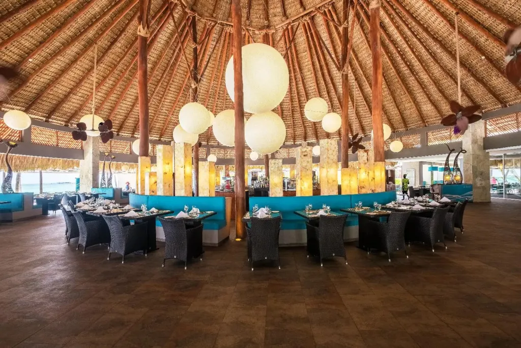 Une salle de restaurant lumineuse avec des tables dressées et un décor tropical.