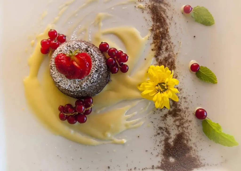 Un dessert au chocolat est décoré de fruits rouges et d'une crème jaune.