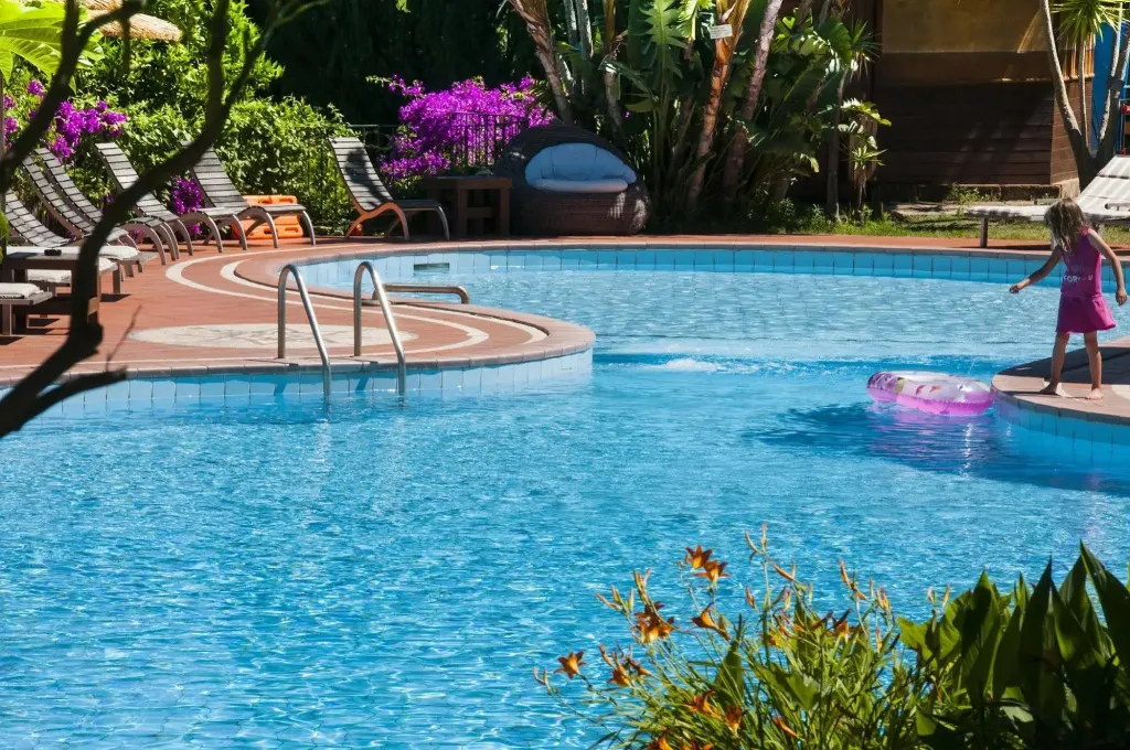 Une piscine ensoleillée avec des transats et une personne près du bord.