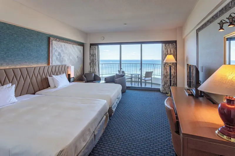 Chambre lumineuse avec vue sur la mer depuis un balcon.