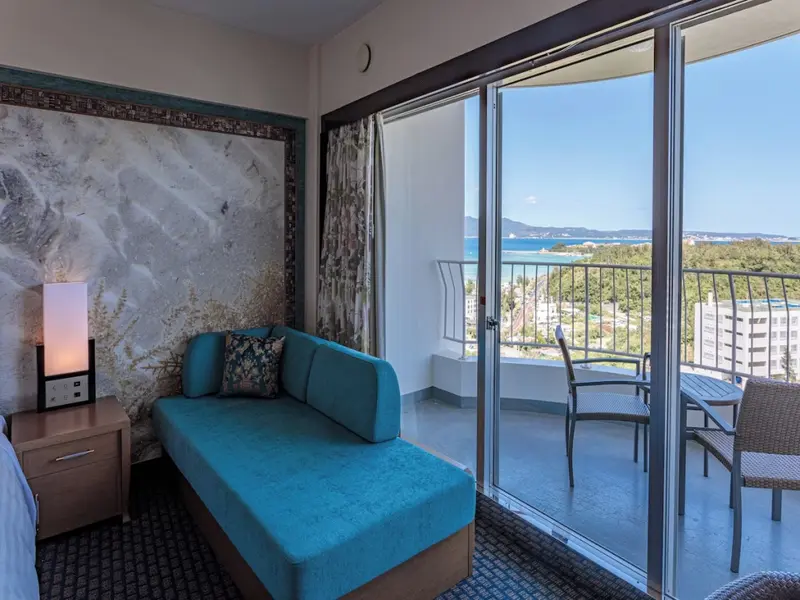 Espace de détente intérieur avec canapé turquoise et vue sur la végétation et la mer.