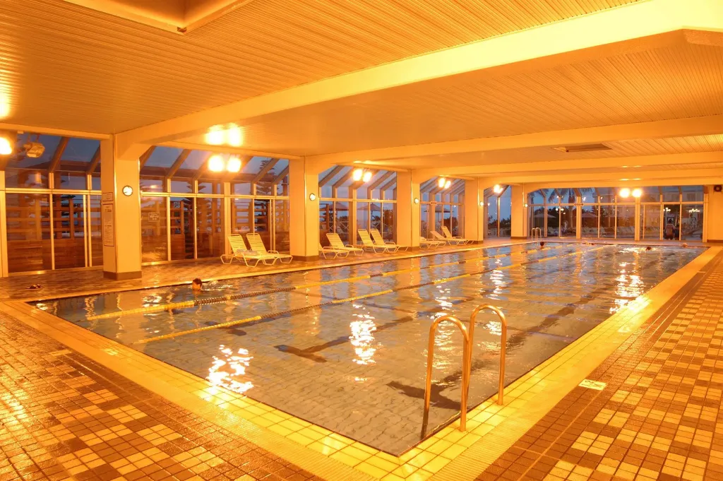 Une piscine intérieure lumineuse avec des transats alignés le long des baies vitrées.