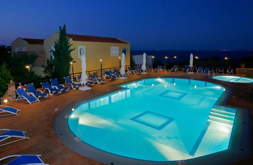 Piscine illuminée avec transats et bâtiment en arrière-plan au crépuscule.