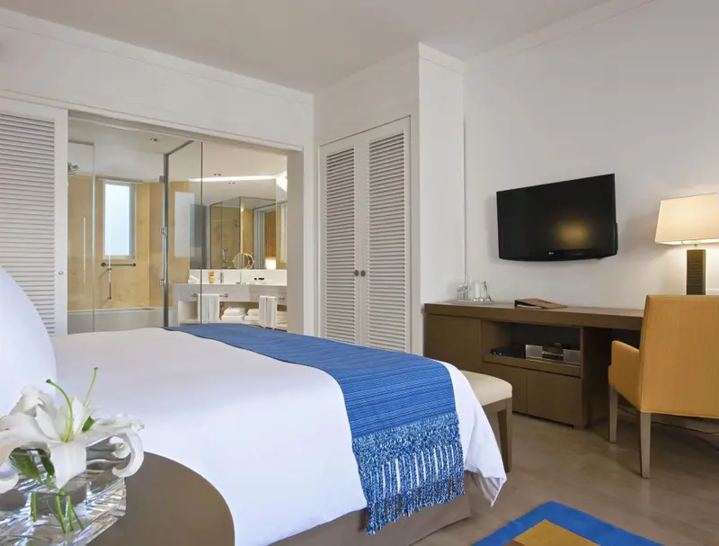 Une chambre lumineuse avec un grand lit et une salle de bain vitrée.