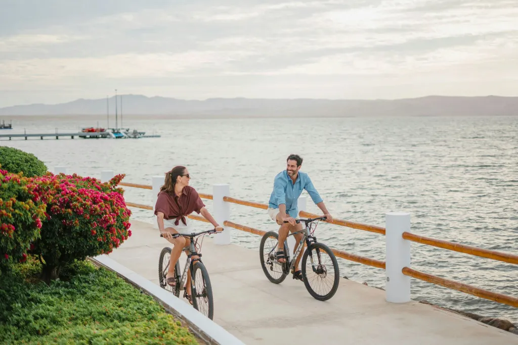 Un couple à vélo longe une promenade fleurie en bord de mer.