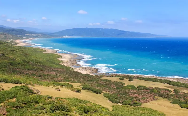 Vue aérienne d'une côte rocheuse bordée de végétation et de montagnes.