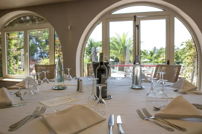 Une table est dressée devant de grandes fenêtres ouvertes sur un jardin luxuriant.