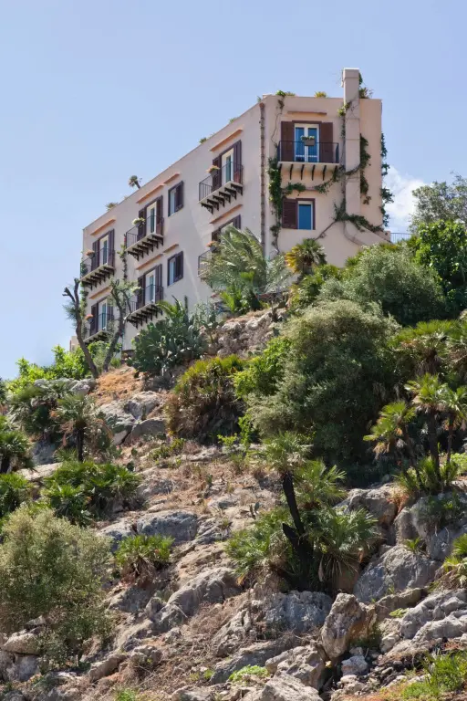 Bâtiment beige aux balcons fleuris perché sur une colline rocheuse.