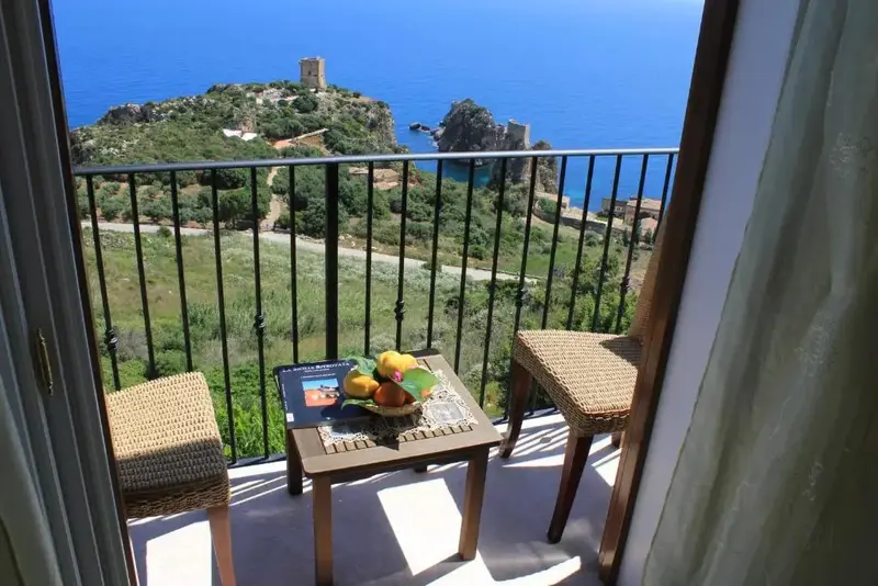 Une table et deux chaises en rotin sont disposées sur un balcon avec vue sur la mer et la côte.