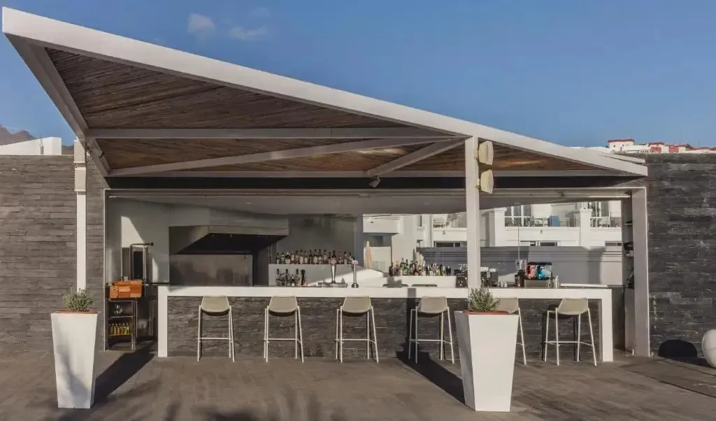 Un bar extérieur avec un comptoir et des tabourets sous une structure en bois.