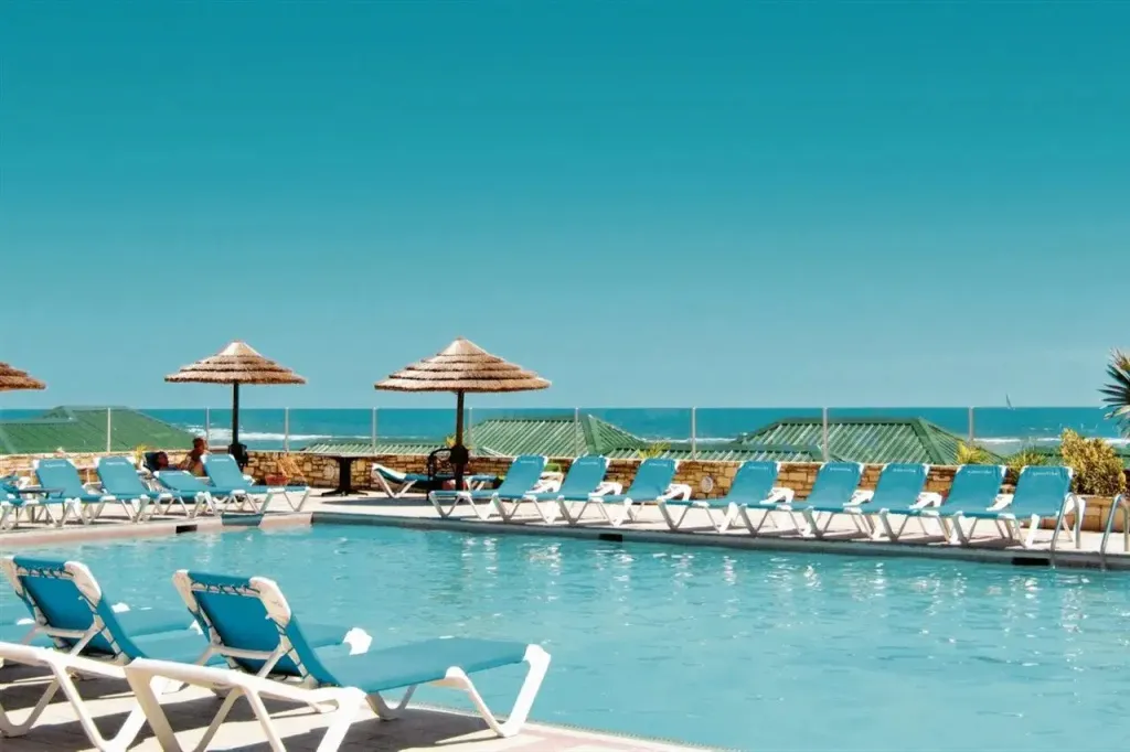 Transats bleus alignés au bord d'une piscine ensoleillée avec vue sur la mer.