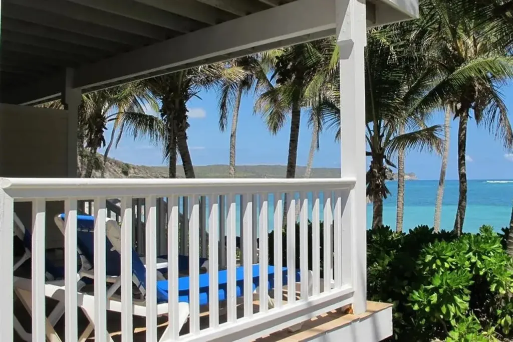 Terrasse avec transats blancs donnant sur une plage de sable fin et la mer turquoise.