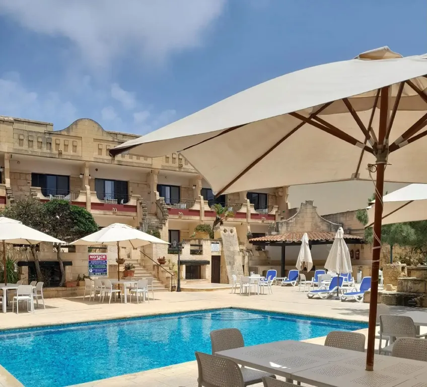 Une piscine ensoleillée avec des transats et des parasols devant un bâtiment à plusieurs étages.