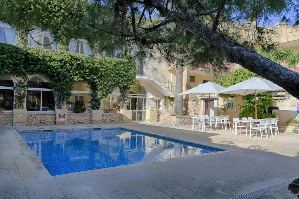 Une piscine rectangulaire bordée d'une terrasse ensoleillée avec des parasols et des tables.