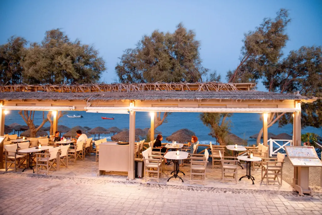 Terrasse de restaurant en bord de mer avec tables éclairées et vue sur la plage.