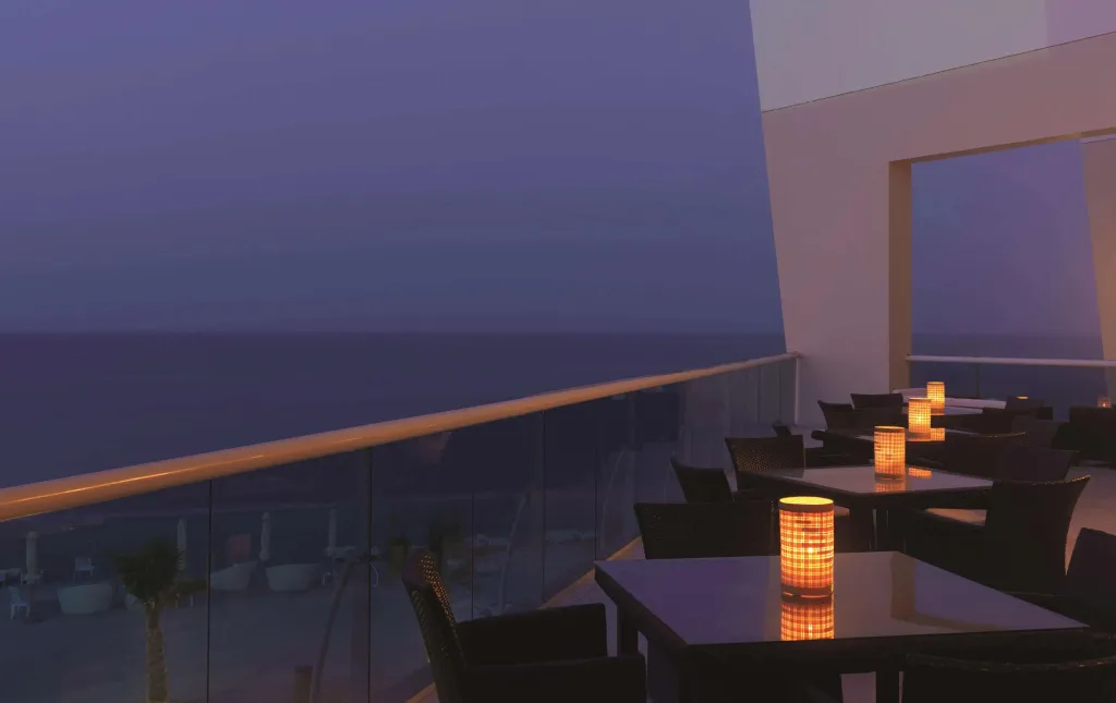 Tables éclairées à la bougie sur une terrasse donnant sur la mer au crépuscule.