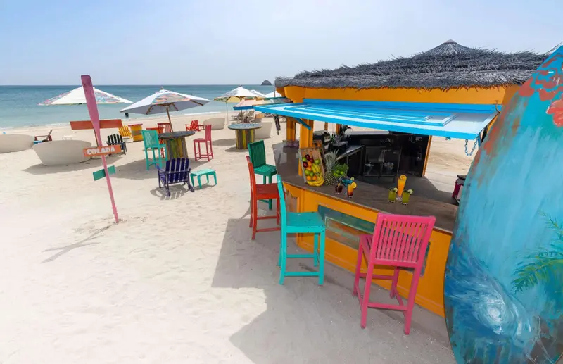 Un bar de plage coloré s'ouvre sur une plage de sable blanc et une mer turquoise.
