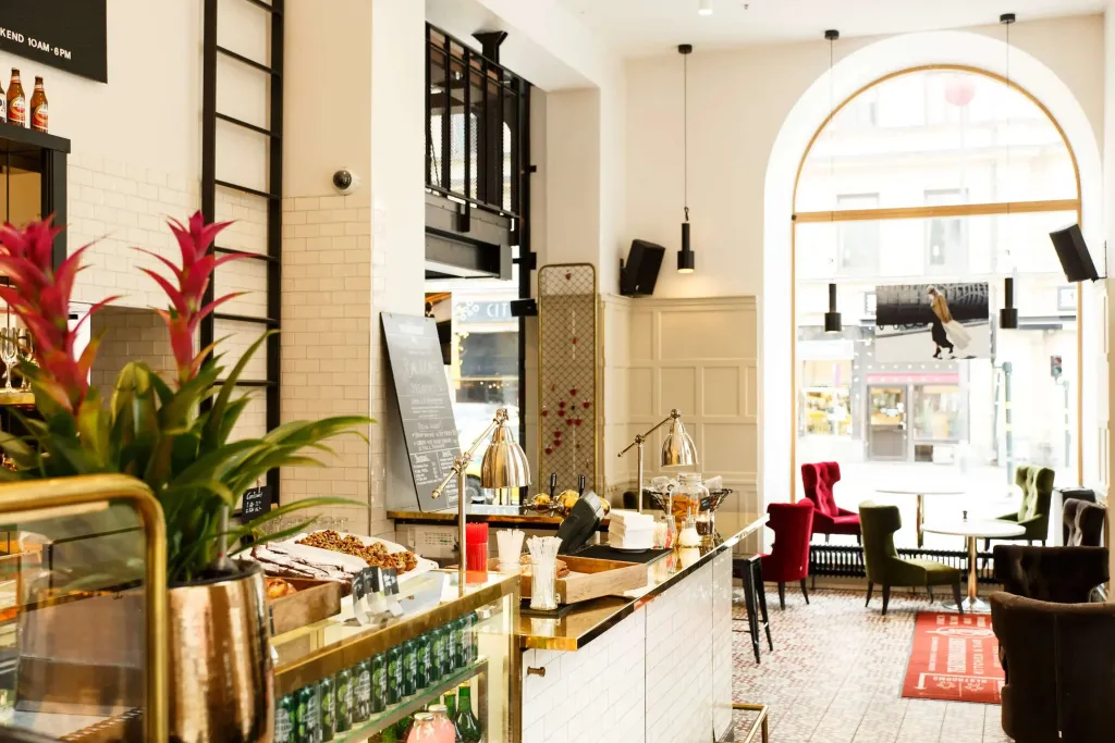 Un comptoir de buffet garni de pâtisseries et de boissons se trouve dans un espace lumineux avec des tables et des chaises.
