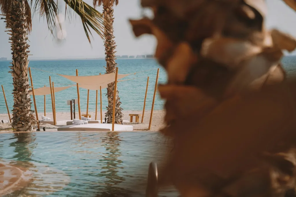 Une plage de sable clair avec des transats et des parasols à l'ombre de palmiers.