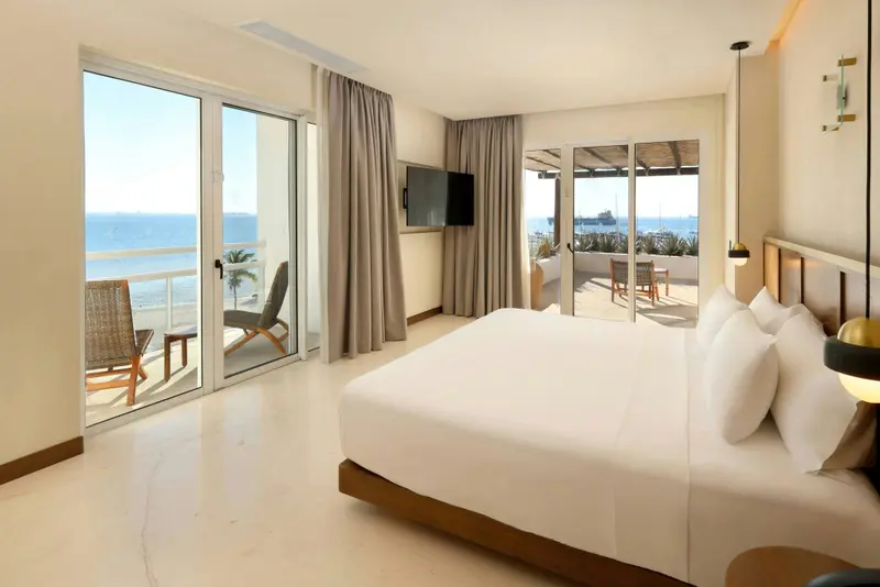 Une chambre lumineuse avec un grand lit blanc donnant sur une vue mer.