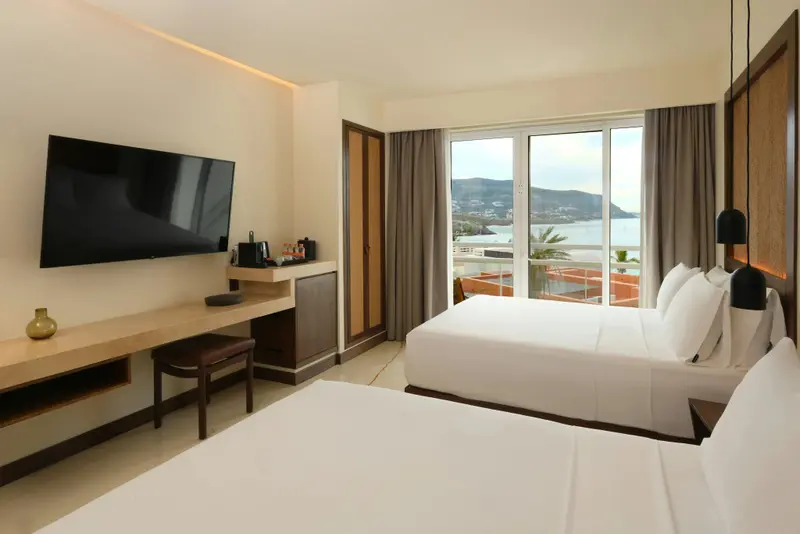 Une chambre lumineuse avec deux lits et une vue sur la mer par de grandes baies vitrées.