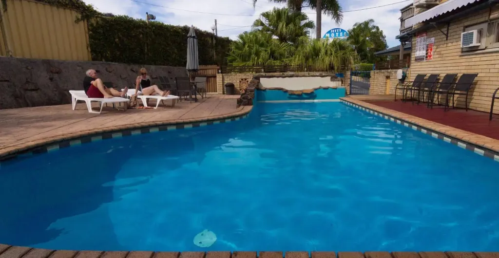 Une piscine turquoise bordée d'une terrasse en bois avec des transats.
