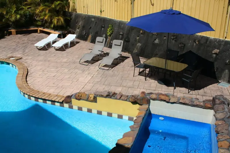 Terrasse avec transats et table ombragée près d'une piscine.