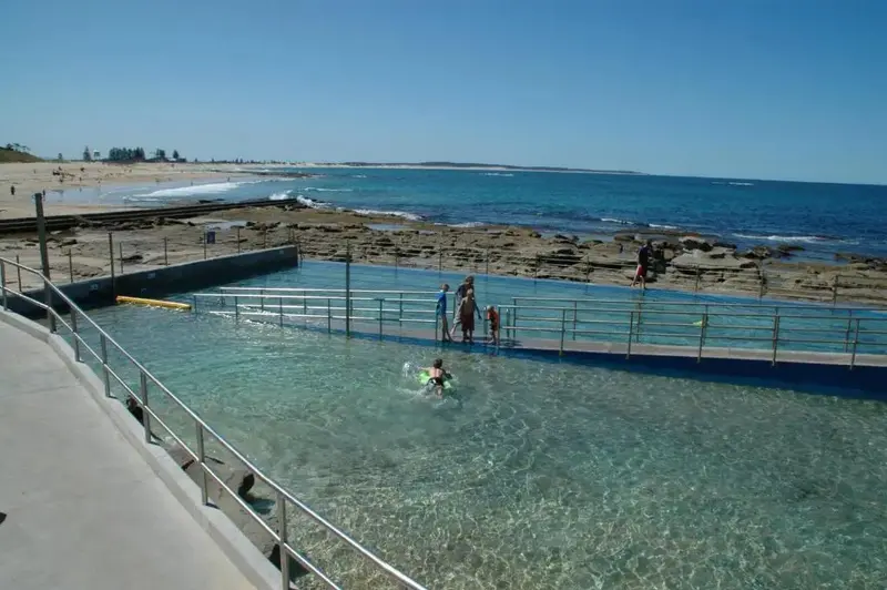 Une piscine naturelle bordée de rochers offre un espace de baignade face à l'océan.