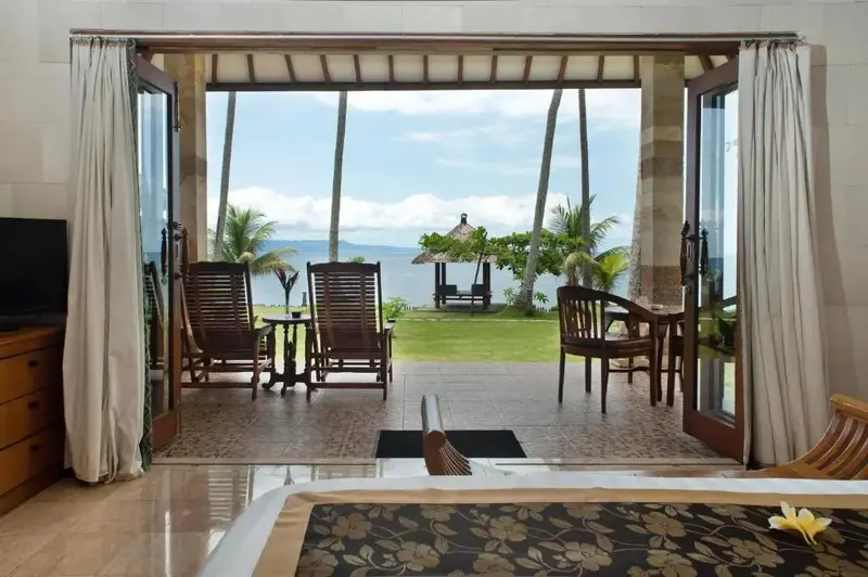 Une chambre s'ouvre sur une terrasse avec vue sur la mer et la végétation.