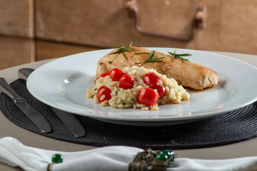 Assiette de risotto aux tomates cerises et un morceau de poulet grillé.