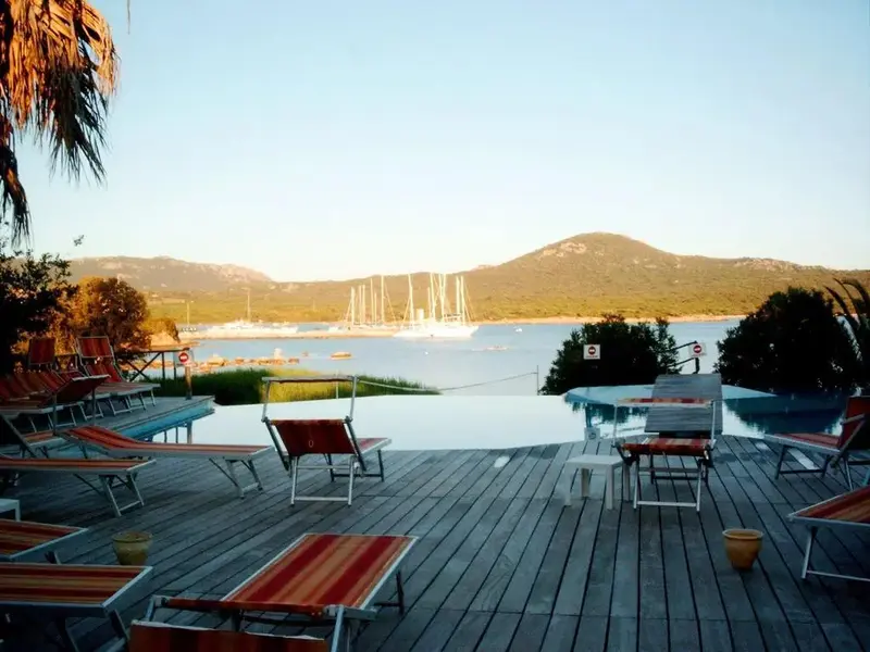 Terrasse en bois avec transats donnant sur une piscine à débordement et une baie.