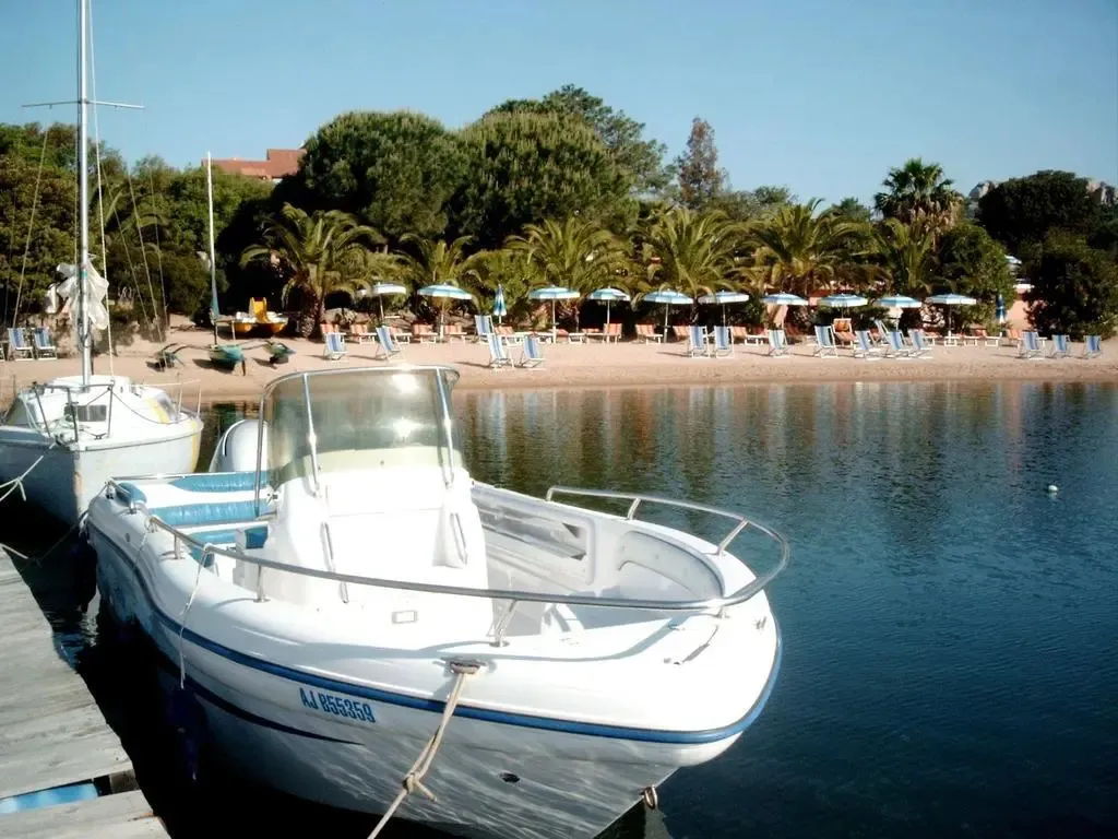Une plage de sable fin bordée de transats et de parasols, avec des bateaux amarrés au premier plan.