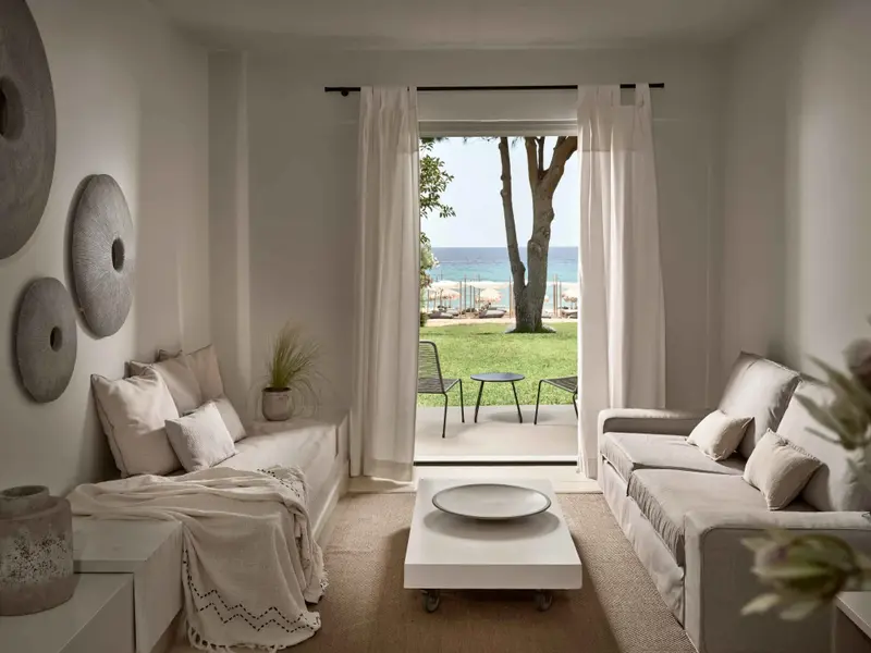 Espace de détente lumineux avec canapés et vue sur une pelouse verdoyante menant à la mer.